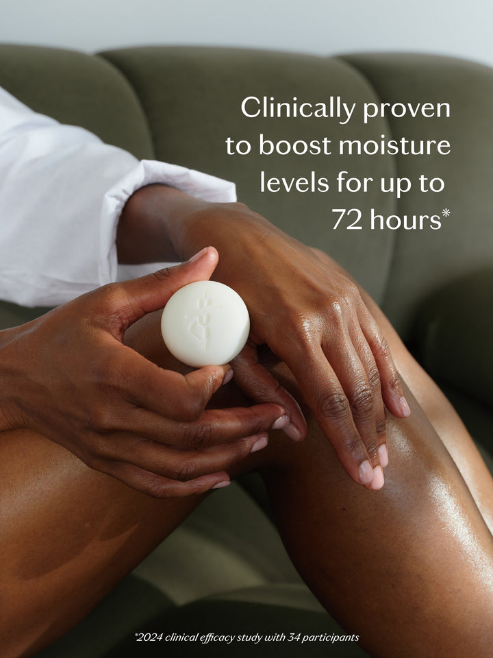 A person applying a white circular cosmetic product to their leg while sitting on a green couch. White text on the image reads: 'Clinically proven to boost moisture levels for up to 72 hours'.