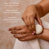 A person's hands apply a white oval body stone with a geometric star design onto their wrist, demonstrating its use. The image includes a 'How to Use' text overlay on the left, set against a warm beige background with a white textured towel.