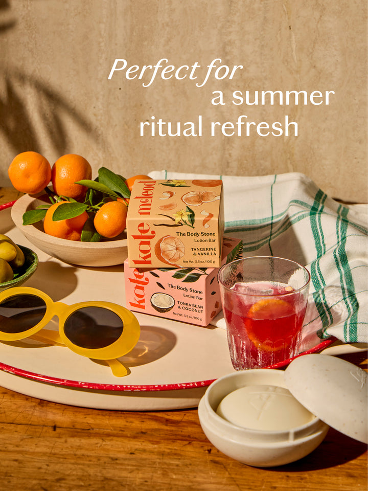 Summer limited edition Body Stones in a summer-themed setting with Travel Case, oranges, sunglasses, and a glass of iced tea on a wooden table. Perfect for a summer refresh.