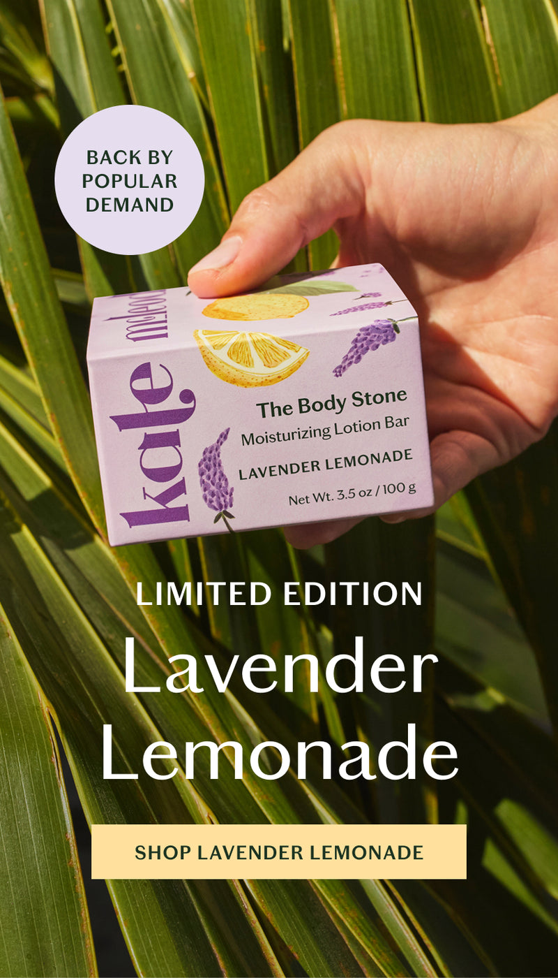 A refreshing take on summer, limited-edition Lavender Lemonade blends herbaceous lavender with bright, zesty lemon. Holding the body stone in its lavender and citrus packaging on a background of palmetto leaves.