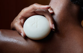 A close-up of a person holding a round recovery stone body stone against their shoulder, with the back of their neck and upper shoulder visible.