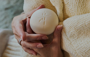 A close-up of a person's hands holding Kate McLeod Body Stone wrapped in a cozy cream-colored knit sweater.