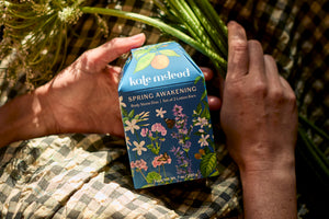 Hands holding Spring Body Stone Duo against gingham and flowers background.