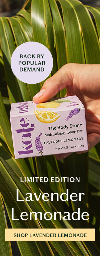 A refreshing take on summer, limited-edition Lavender Lemonade blends herbaceous lavender with bright, zesty lemon. Holding the body stone in its lavender and citrus packaging on a background of palmetto leaves.